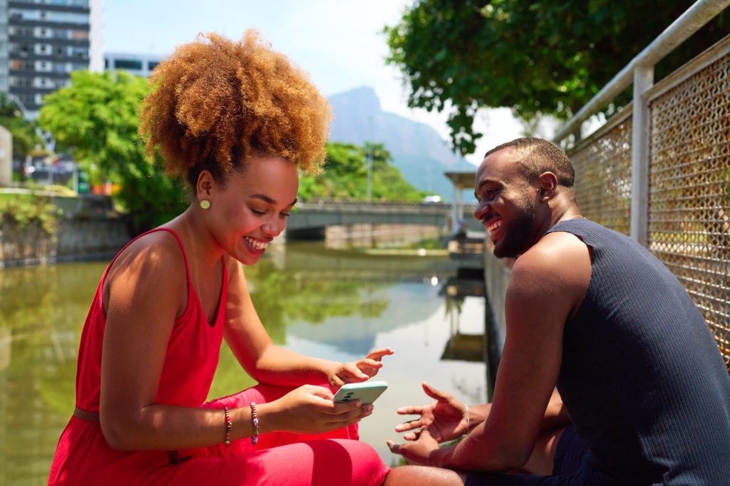 afro black brazilian heterosexual couple using cell phone interacting outdoors